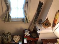 Various wood, ceramic and decorative items arranged on and around shelves. Includes figurines, plates, and dried grass bundle.