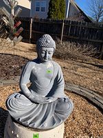 Front view of Buddha garden sculpture seated on a stool with chipped white paint on grey surface.