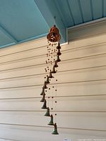 Full view of the Cuban bells mobile hanging showing the top wooden piece and multiple ceramic bells suspended on strings with wooden beads.