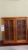 Front view of wooden curio cabinet with glass panel doors and metal pulls.