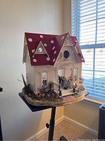 View of handmade dollhouse from a side angle showing the red polka dot roof, windows, porch, and detailed garden base