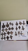 Overview of 25 Ethiopian metal pendants pinned to white board showing variety of styles including crosses and star shapes