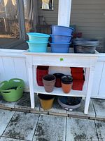 Overview photo showing white plastic flower box with shelf, multiple plastic pots in blue, black, red, brown, orange, yellow, and gray colors.