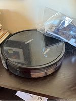 Black DEEBOT robotic vacuum cleaner with transparent top plate showing dust specks, on wooden surface.