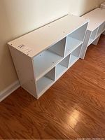 White rectangular shelf unit with six equal open compartments, angled view showing depth and top surface with screw holes.