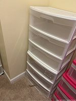 Two stacked white plastic storage containers with three drawers each in a corner of a room on carpet.