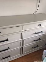 View of the antique white dresser showing black metal drawer handles and knobs, detailed panels on drawer fronts.