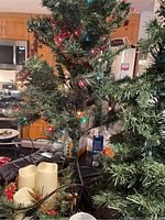 Photo of 3 ft artificial Christmas tree with colorful lights and holiday decorations on table including flameless candles and ceramic mug.