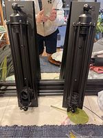 Photo showing two black cast iron industrial style wall light fixtures standing upright on a surface in front of a mirror. Fixtures are tall, narrow, with cage-like enclosure and rotatable joint near top.