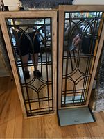 Pair of two wood-framed mirrors with black decorative iron grids placed adjacent to each other on a wooden floor.