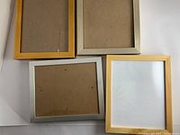 Set of four 8x8 wooden picture frames in gold, silver and wood finishes, laid on white background showing front and back sides.