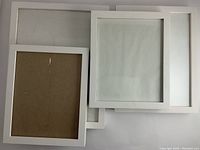 Top view of four white wooden frames stacked, showing front and back sides, clean glass and white frames