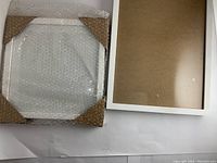 Four white wooden picture frames with glass and backs visible, some wrapped with bubble wrap and cardboard corner protectors.