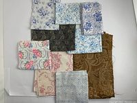 Full view of multiple antique cotton fabric remnants arranged flat on white surface, showing various colors and patterns including blue floral, brown and black paisley, and pink florals.