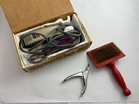 Photo of the animal clipper trimmer in original box with power cord, nail clipper, and dog brush arranged side by side.