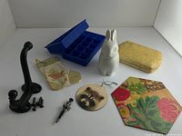 Full lot view showing all items: white ceramic bunny piggy bank, blue silicon ice trays, raccoon ornament, floral wine bottle coaster, mini Xmas stocking, cast iron coat hook, brooch, watch box.