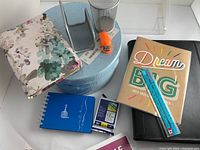 Photo showing set of 3 blue round hat box style boxes, floral folder, metal pencil cup, small orange stapler, blue notebook, ruler and large black binder.