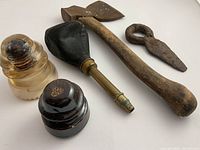 Group photo of all antique tools showing axe, brass horn part, iron eye piece, glass and porcelain telegraph insulators.