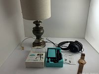 Overall shot of the lot items on white background, including lamp, headphones, tripod in packaging, and men's bamboo watch.