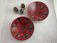 Top view showing two red pottery bowls with vivid abstract patterns and three greenish tea cups grouped together on a white background.