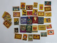 Top-down photo showing all 7 mid-century and vintage matchbooks stacked and arranged, showing colorful printed designs and logos from various hotels and safety matches primarily from India and USA.