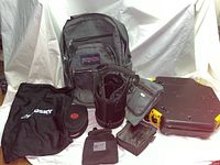 Overview photo showing all items in the lot including backpacks, beverage holder, small pouches, and hard plastic container