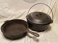Cast iron Dutch oven with lid and handle, and a deep cast iron pan side by side showing overall condition.