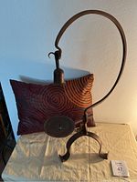 Cast iron candle holder in front of decorative red pillow with swirls.