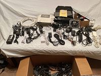 Overview of cords, adapters, small fans, lights, antenna, and other electronics on a white cloth covered surface.