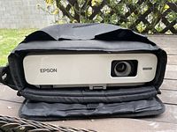 Front view of the Epson projector inside the black padded carrying case, showing the lens and Epson branding on the white front panel.