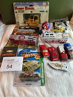 Photo of entire lot showing John Deere bulldozer in package, Cubs car, multiple toy vehicles including Hot Wheels, Matchbox, NASA vehicle, and small boats.