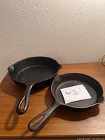 Two vintage cast iron Griswold skillets side by side on wood surface showing handles and overall shape.