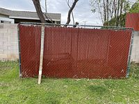 Full view of one 6ft fence panel with red vinyl slats leaning against block wall