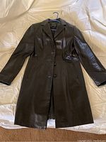 Full view of black leather long coat with side pockets, button front, laid flat on a surface