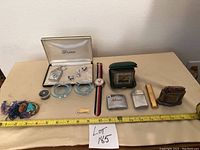 Wide shot of entire lot on table showing ashtrays, lighters, clock, watch, brooch, jewelry and pins with measuring tape