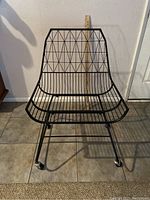 Front view of the black wire metal chair showing geometric pattern and casters.