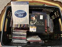 Basket containing over 50 music CDs and 3 DVDs with visible titles including American Idol and Act of Valor.