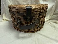 Front view of the woven wicker picnic basket showing leather handle and metal closure latch.