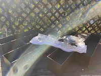 Set of six black rectangular plastic planter boxes arranged outside with some plastic bags on top.