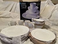 Complete 16-piece Studio TU Otella bone china dinnerware set with cups, bowls and plates, still partially wrapped in packing materials next to the boxed set.