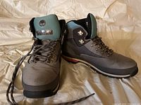 Front and side view of Timberland hiking boots with cleated black sole, patterned laces, and teal padded collar