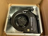 Metal ventilation fan in cardboard box showing blower wheel and motor assembly.