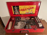 Photo of the opened red metal case showing original Sensational New Erector label inside lid, various metal parts and running electric motor inside compartments.