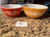 Two vintage Pyrex bowls side by side on a countertop showing red wheat design and yellow floral design.