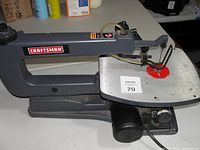Full side view of gray Craftsman scroll saw with flat worktable and red blade insert, showing on/off switch and power cord.