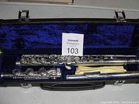 Flute disassembled inside a black hard case lined with blue velvet, includes a yellow cleaning cloth.