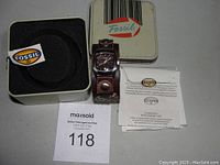 Overall view of Fossil watch with original tin box and paperwork on white background, including auction lot number.