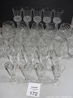 Overview of 21 crystal glasses of various sizes and styles arranged on a black background, showing the etched designs on the glass surfaces.