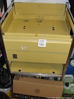 Front view of the yellow metal medical cabinet showing the main compartment with drilled holes on the top panel and drop-down door below.