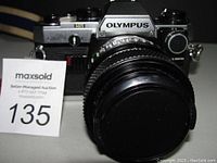 Front view of Olympus OM-10 SLR camera with attached lens and lens cap